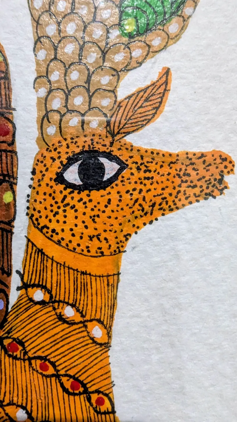 A folk-art painting of a deer in orange and gold, patterned with eyes